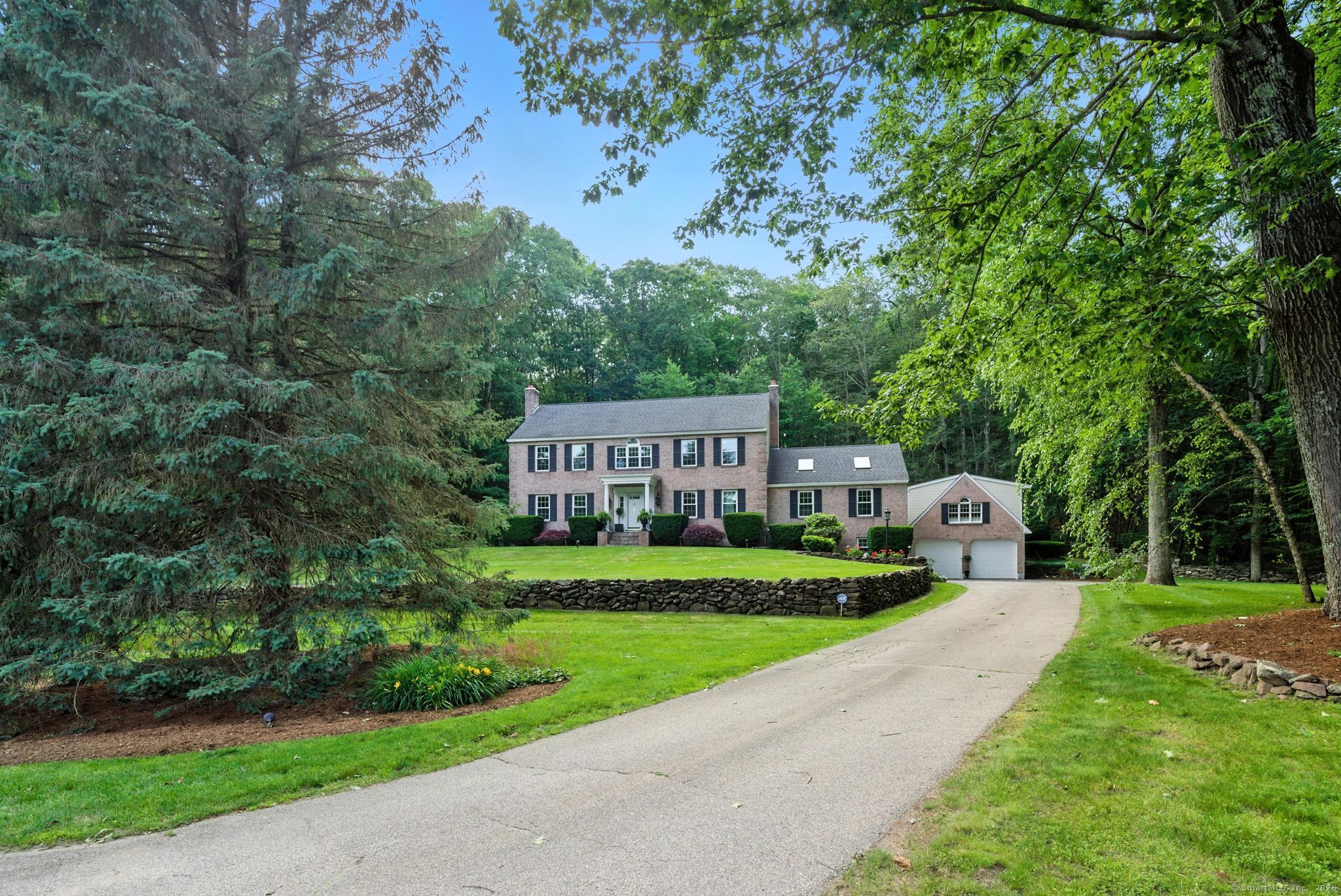 Experience refined New England living in this masterfully crafted colonial, set on 1.36 beautifully landscaped acres in one of Bolton's most desirable cul-de-sac neighborhoods. From the moment you arrive, you're welcomed by stone walls, a brick facade, a pillared front porch, and a transom-topped entry door that hints at the sophistication within. Rich hardwood floors with intricate inlays, extensive crown and panel moldings, and custom millwork create a seamless blend of elegance and warmth throughout the home.  The gourmet kitchen is a chef's dream, featuring custom full inlay red birch cabinetry, sleek black granite counters, a stunning center island with wine cooler, and premium appliances. It continues seamlessly to the formal DR & Inviting sunroom. The great room impresses with cathedral ceilings, a striking native brownstone Rumford FP, and bespoke built-ins. French doors open to a vast paver patio and a spectacular terraced garden, illuminated by 16 custom copper and steel torches-perfect for unforgettable outdoor gatherings.  Upstairs, retreat to a spacious primary suite w/ a skylit spa-like bath, alongside 3 generous bdrms, a designer full bath, and a separate laundry room. The finished lower level offers a kitchenette, matching millwork, durable epoxy flooring, & an office/media rm, & excellent storage. A detached heated carriage house with a game room and contractor-height garage adds flexible luxury. Minutes to Case Mountain trails, Bolton Lake, UCONN & Hartf
