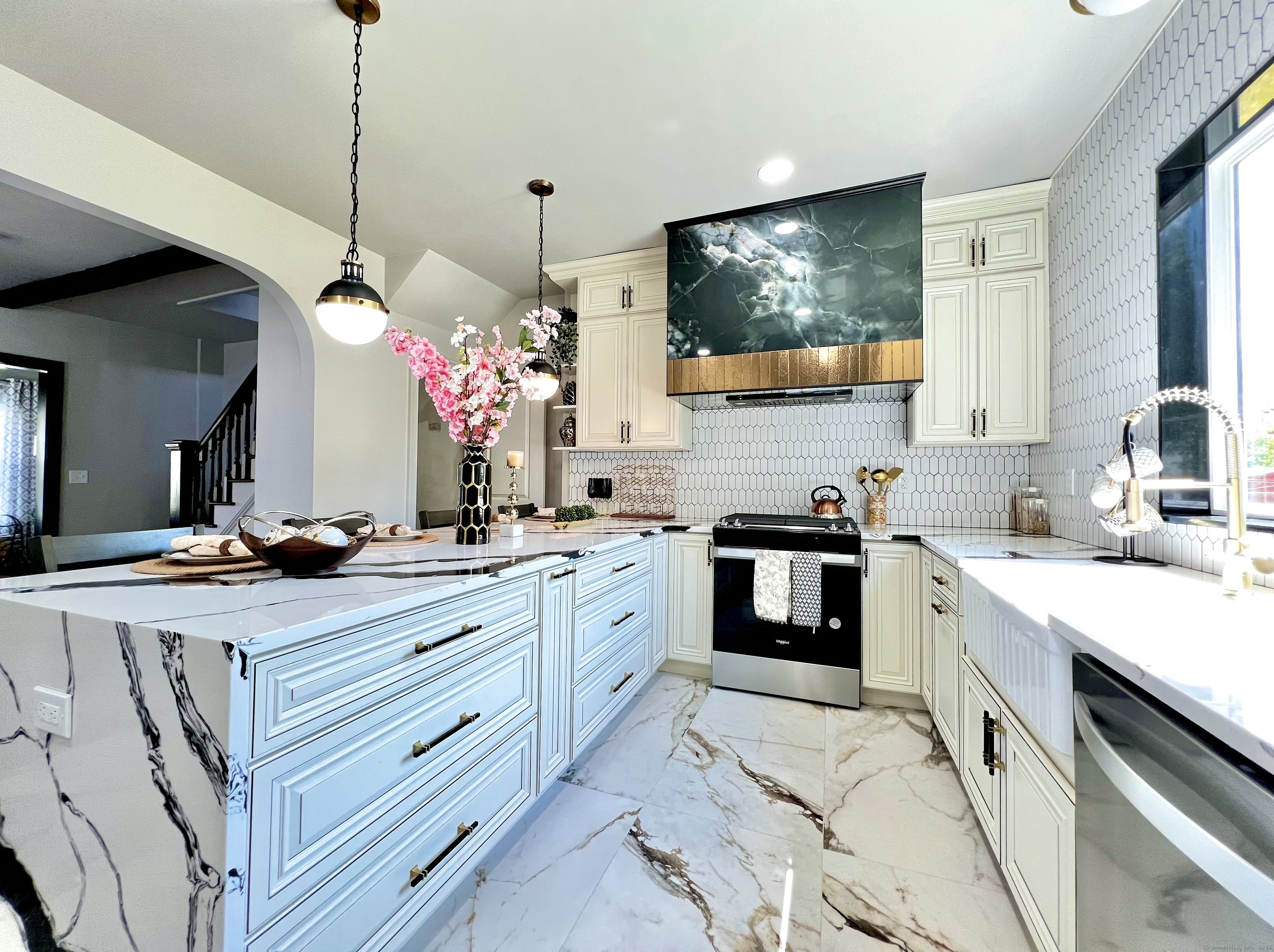Renovated kitchen with a marble-patterned island, green stone range hood, and hexagonal tile backsplash.