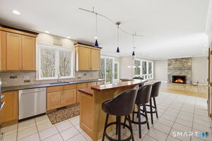 Custom shaker style solid maple cabinets with subway tile backsplash and quartz countertops and neutral tile floor create a timeless vibe for this kitchen. The fireplace can be seen from the kitchen, informal dining area and living room.