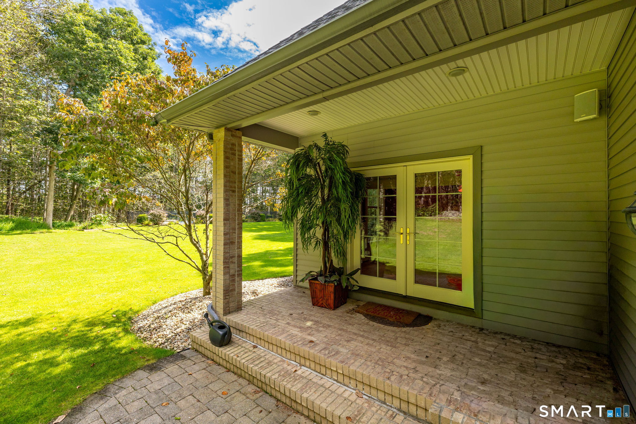 This is the covered porch area from the french doors of the sunroom, with classic brick flooring, lighting, and a speaker to keep the fun going outside.