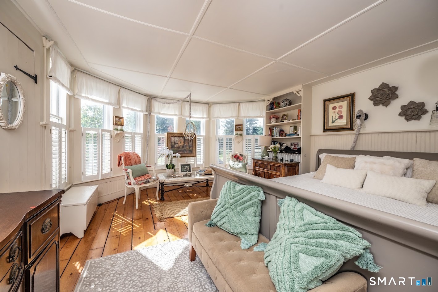 Spacious primary bedroom filled with natural light, featuring hardwood floors and a beautiful bay of windows with interior shutters.
