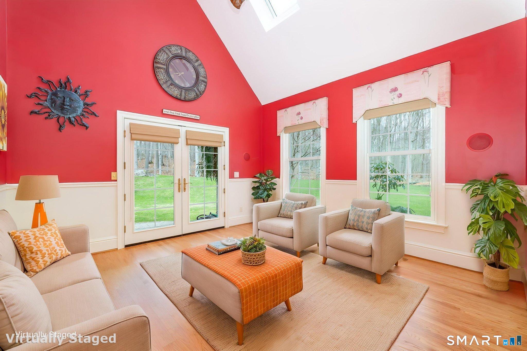 The 13'7" x 15'6" sunroom with soaring vaulted ceilings, skylights installed in October 2024, oak floors refinished December 2025, chair rails, French doors leading to a covered brick porch, ceiling fan, and custom window treatments.