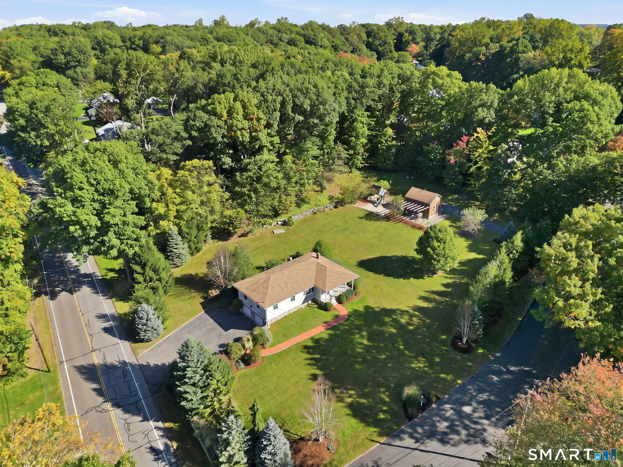 Mornings here start w/ birdsong from the mature trees &, on a good day, a fox or a few deer crossing the yard. Set on a one-acre corner lot framed by professional landscaping, this home offers privacy & calm, w/ Tashua School's playground & fields a short walk away. The exterior was rebuilt to last: Maibec cedar shake siding, Azek trim, 4" stone veneer & Andersen windows & doors. A brick walkway leads to the bluestone front porch, an easy spot for morning coffee or a quiet evening. Inside, natural light moves across hardwood floors through most of the main level. The living room is anchored by a large picture window, & a separate family room gives everyone a place to settle in. The kitchen offers white cabinetry, granite counters, stainless appliances, & a dining area. The mudroom opens to a private bluestone patio made for summer evenings & time w/ friends. Three well-sized bedrooms sit at the end of the hall, including a primary suite w/ its own full bath. A full hall bath serves the other bedrooms & guests. The finished lower level adds porcelain-tiled living space, a half bath, laundry, & access to the large two-car garage. Electrical upgrades & a newer water heater add peace of mind. A detached outbuilding finished in cedar shake & stone veneer, w/ water & electric, is ready to become an office, gym, or studio. Quiet roads for bike rides & walks, among the first cleared after a storm, complete a ranch-built w/ intention, on land that feels like your own retreat.