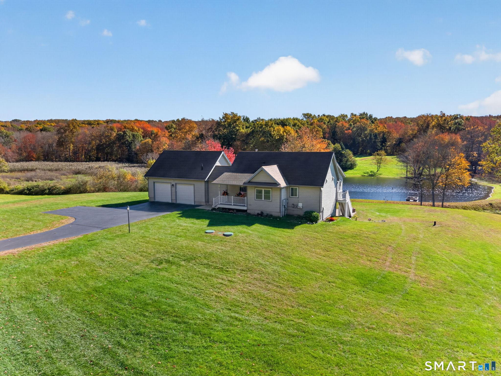 Discover this distinctive country retreat on 5+ picturesque acres, featuring a custom-built home with approximately 2,264 finished square feet, 3 bedrooms, and 2.5 baths. The main level living room boasts a cathedral ceiling, wood stove, and hardwood floors. The dining room features built-in cabinetry, while the kitchen offers granite countertops, a center island, custom cherry cabinetry, and a spacious walk-in pantry with a secondary sink. Enjoy scenic views of the private pond and landscape from the living room and sunroom. The main-level primary suite features French doors and a full bath. Two additional lower-level bedrooms offer French doors and direct patio access and one includes an en-suite bath. A walk-out basement provides convenient access to the outdoors, while the oversized two-car garage offers ample space for storage. The property's outdoor amenities are equally appealing, highlighted by a private spring-fed pond spanning approximately 1.25 acres with an estimated depth of 13 feet. An expansive patio, timber pavilion, and covered porch create inviting settings for outdoor dining, entertaining, or simply enjoying the peaceful surroundings. A solar array and standby generator provide additional utility and resilience. Perfect as a year-round residence, weekend retreat, or multi-generational home, this property offers privacy, flexible living spaces, and a peaceful rural setting while retaining driving access to Boston, Providence, and New York City.