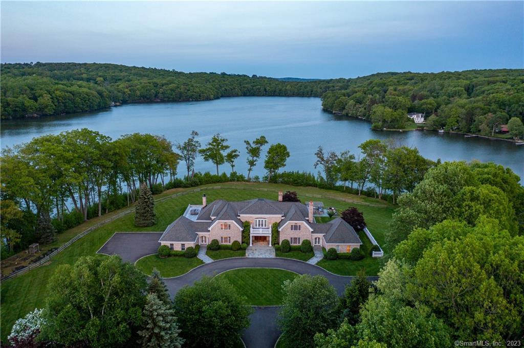 Welcome to 15 Taunton Lake Road! A stately tree-lined drive leads to this stunning estate on Taunton Lake situated on a private peninsula with 900 feet of shoreline and 180 degree lake views. The front entry opens into a grand double height living room and dining room with floor to ceiling windows and three sets of French doors to the terrace overlooking the lake. A chef’s kitchen with Sub Zero, Viking, and Jenn Air appliances and a family room with French doors to terraces on three sides is perfect for everyday living. The fantastic oak-paneled library with a wet bar makes for a great space to quietly read or have cocktails in a more intimate space. Two spacious primary suites are found on the main floor, both with gorgeous lake views. Two more en-suite bedrooms and two spacious home offices are housed in the upper level. The fully finished lower level offers a home gym, a large media room, and a kitchen that leads to the lanai and pool. Outdoor living space includes a heated gunite pool, a Har-Tru tennis court, extensive stone terraces, a fantastically equipped outdoor kitchen, and a dock with electricity. Only electric motors are permitted on Taunton Lake, maintaining serenity and quiet for residents. The stocked lake is a fisherman’s paradise, and a wonderful place to paddleboard, kayak, canoe, and swim. This magnificent estate with exceptional finishes on Taunton Lake is a rare, one-of-a-kind find!